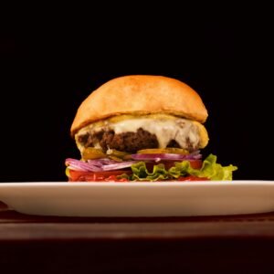 Mouth-watering cheeseburger with fresh veggies and melted cheese on a white plate.