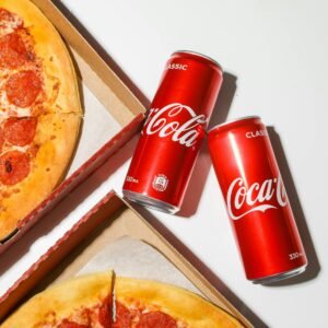 Close-up shot of pepperoni pizza and Coca-Cola cans, perfect fast food combo.