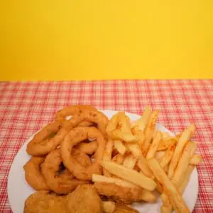 Crispy onion rings, French fries, and nuggets served on a vibrant red plaid tablecloth.